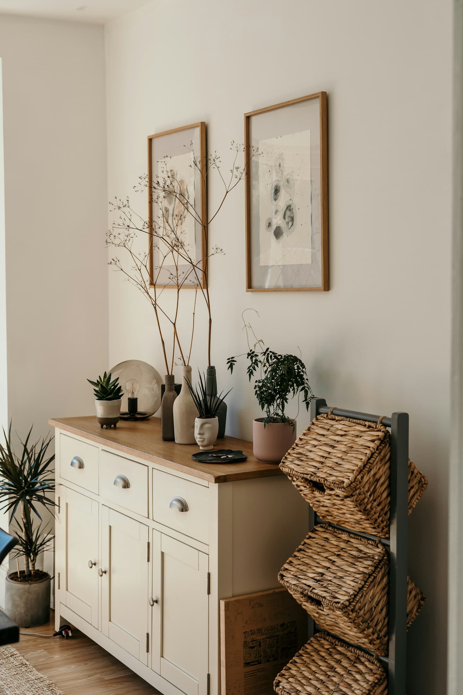 A sunlit living room corner with a low cabinet, woven baskets and potted plants.